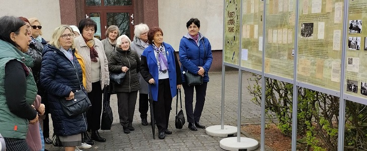 Grupa emerytek ogląda wystawę plenerową.